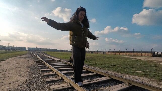 Imagen de una visitante de Auschwitz haciendo equilibrios sobre la vía del tren