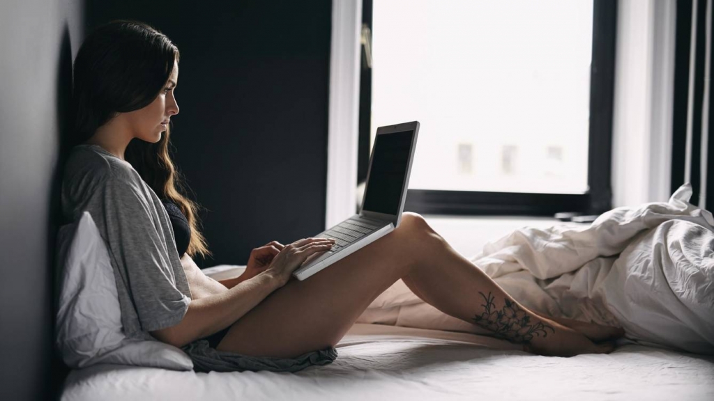 una joven en una cama con un ordenador portátil